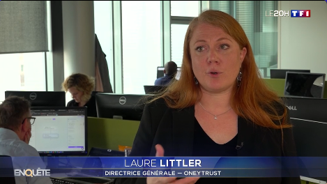 Personne interviewée dans un bureau devant plusieurs écrans d’ordinateur, avec le bandeau de TF1 indiquant une enquête du journal télévisé et le nom et poste de la directrice générale affichés à l’écran. 